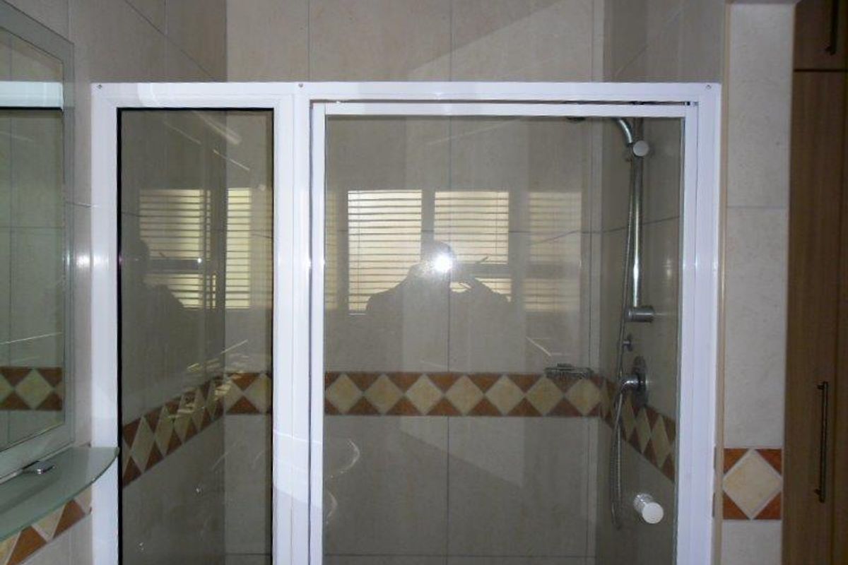 A functional bathroom featuring a glass-enclosed shower with tiled walls and a decorative border, complemented by built-in cabinetry.