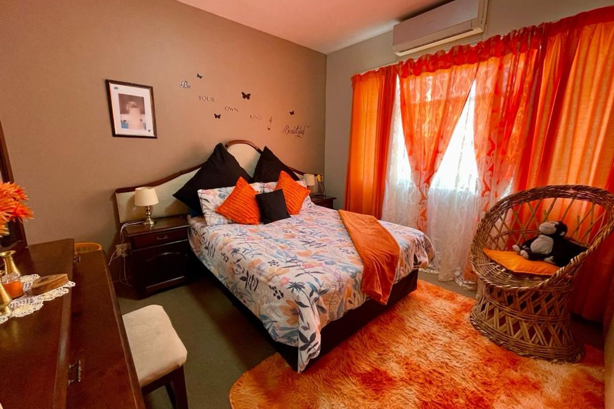 A bedroom featuring a wall-mounted air conditioning unit and large windows with orange curtains.