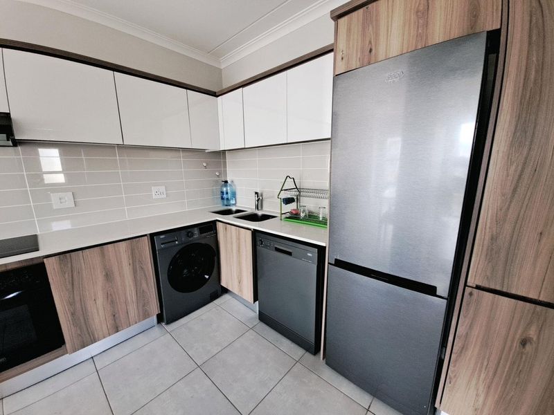 Modern kitchen featuring sleek two-tone cabinetry, stone countertops, tiled backsplash, and integrated appliances, offering a clean and functional workspace.