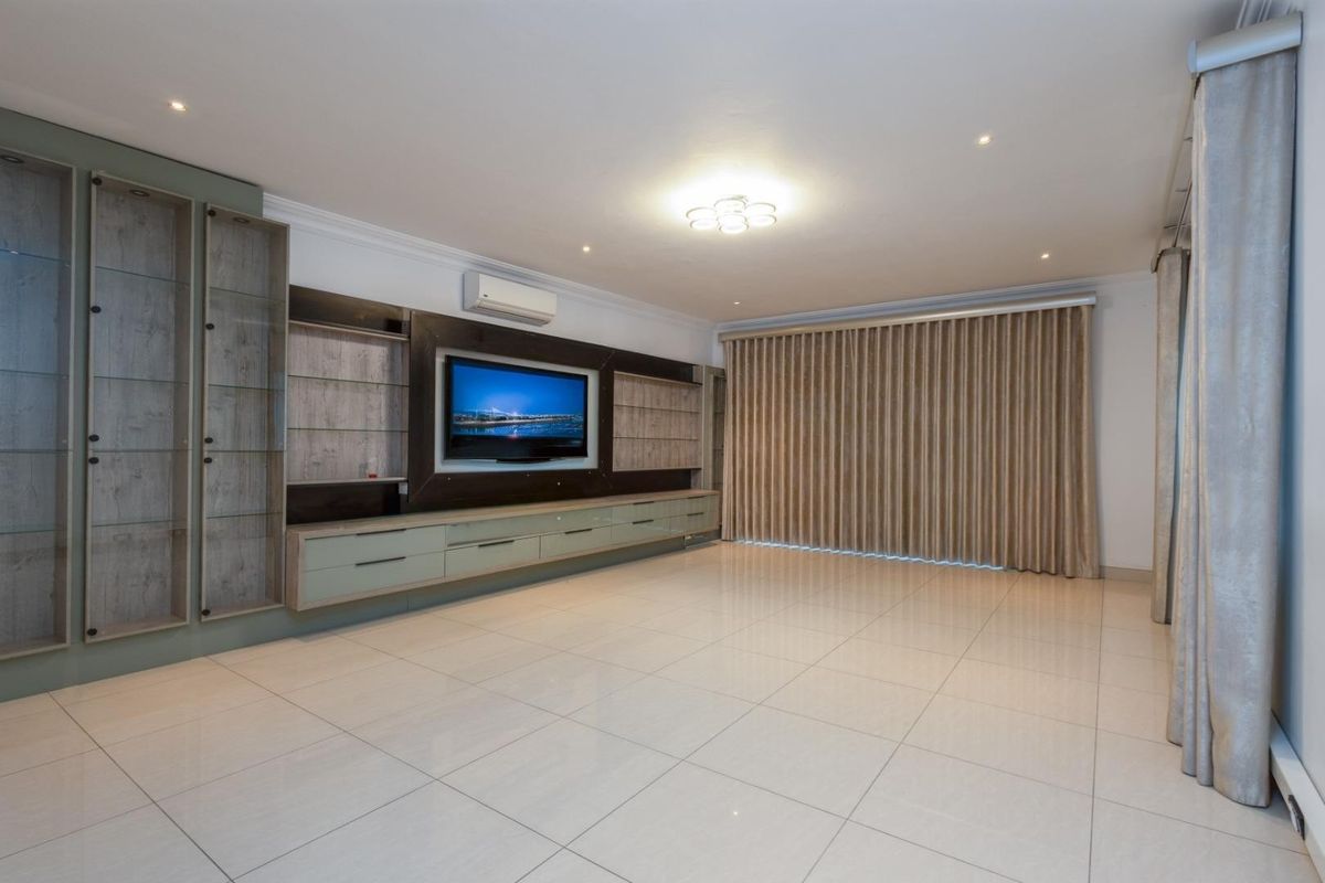 Spacious living room featuring large format floor tiles, extensive built-in cabinetry, and a wall-mounted air conditioning unit.