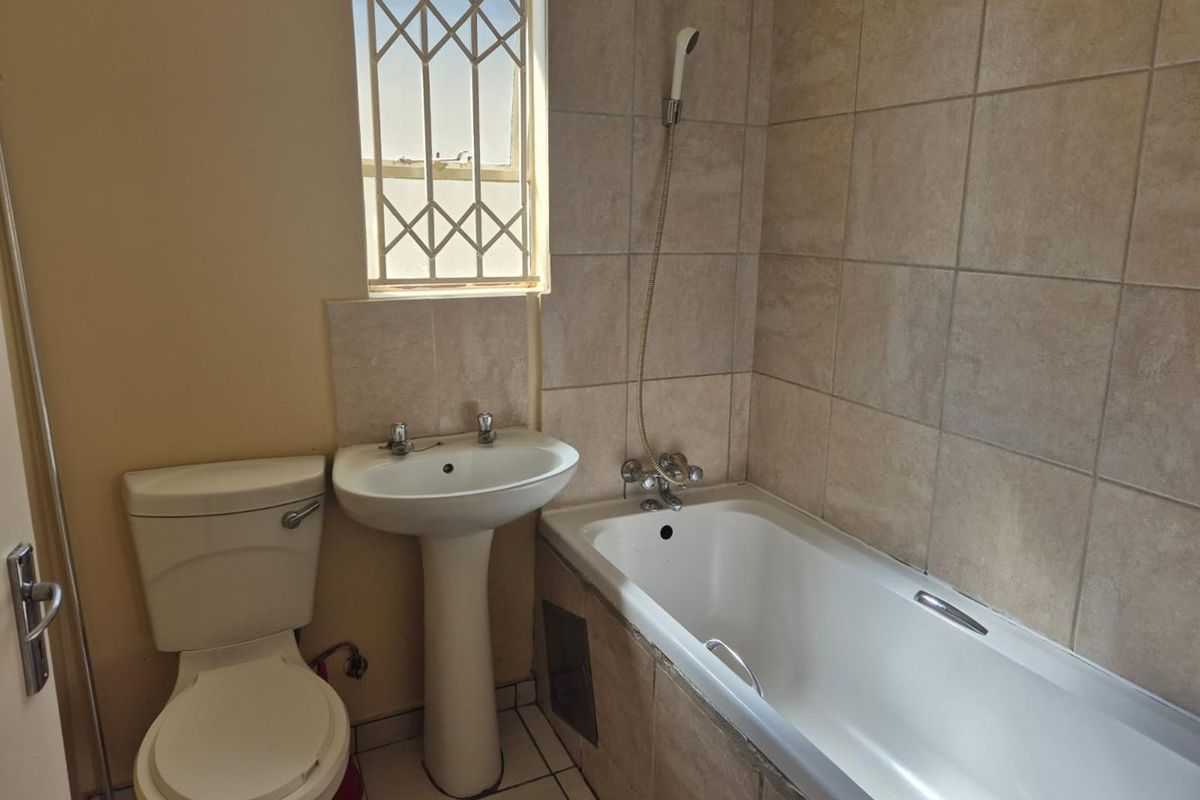 A functional bathroom featuring a pedestal basin, a standard toilet, and a bathtub with a handheld shower attachment, finished with neutral wall tiles.