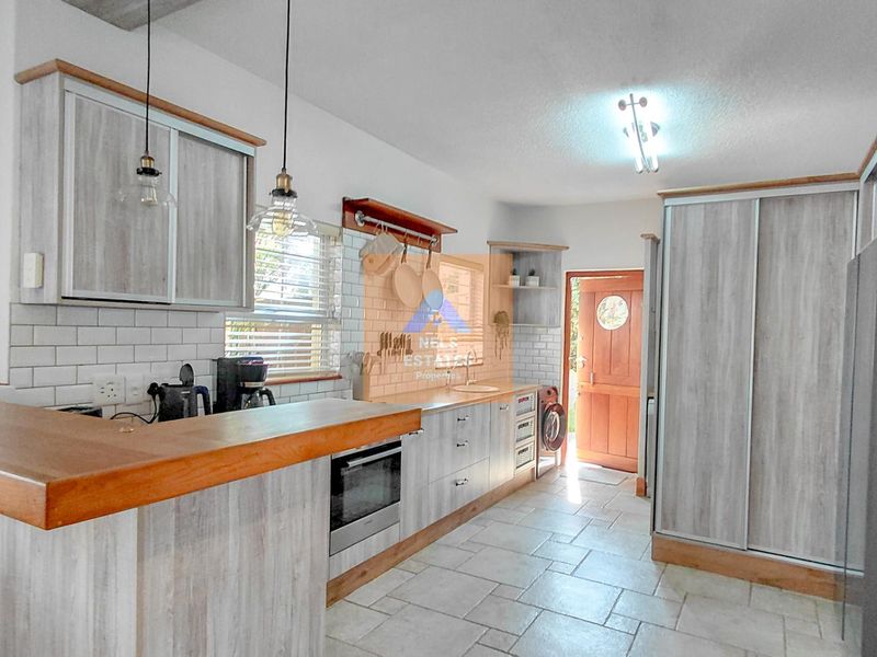 A well-lit kitchen featuring light wood-grain cabinetry, a wooden breakfast bar, subway tile backsplash, and ceramic floor tiles with direct access to the exterior.