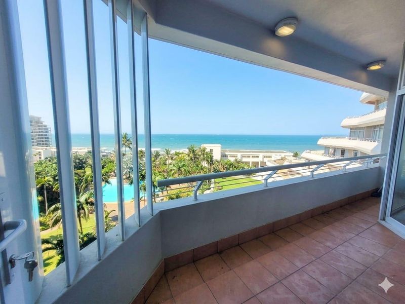 Spacious balcony featuring tiled flooring, metal balustrade, and security bars, offering expansive views of the ocean and complex grounds.