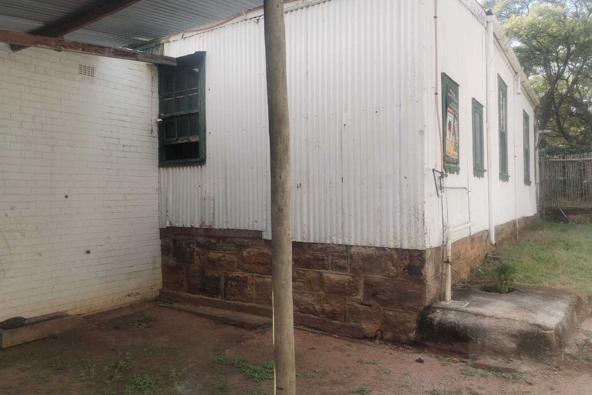Exterior view of a structure featuring a stone foundation and corrugated metal siding, showing significant signs of age and weathering.