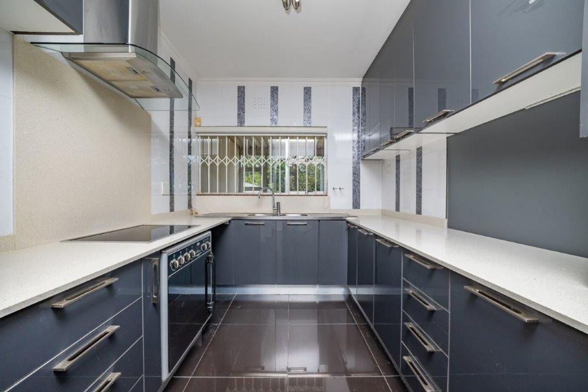 Modern galley-style kitchen featuring sleek grey cabinetry, stone countertops, integrated stainless steel appliances, and tiled flooring.