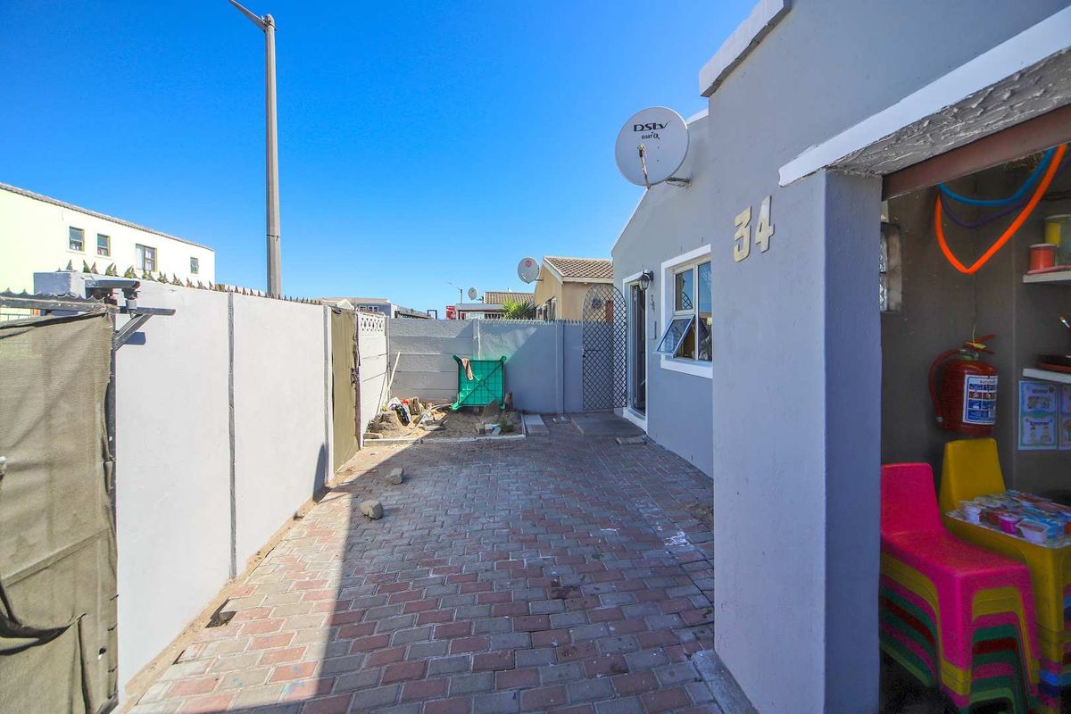 A paved side courtyard area featuring a boundary wall, exterior lighting, and access to the main dwelling entrance.