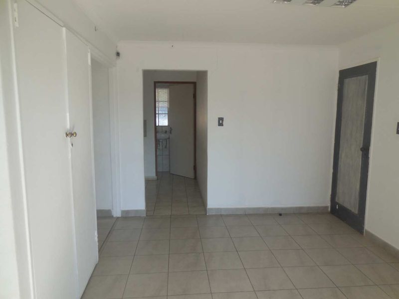 An empty office space featuring neutral tiled flooring, built-in storage cupboards, and direct access to an adjacent washroom area.