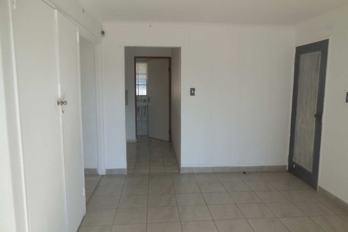 An empty office space featuring neutral tiled flooring, built-in storage cupboards, and direct access to an adjacent washroom area.