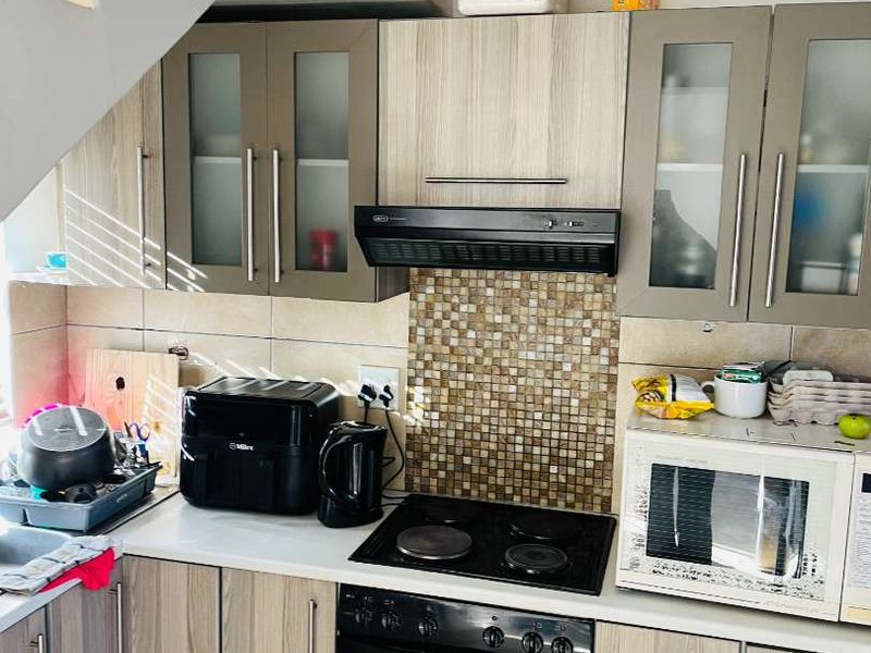 A functional kitchen featuring wood-look cabinetry, mosaic tile backsplash, integrated oven and hob, and an extractor fan.