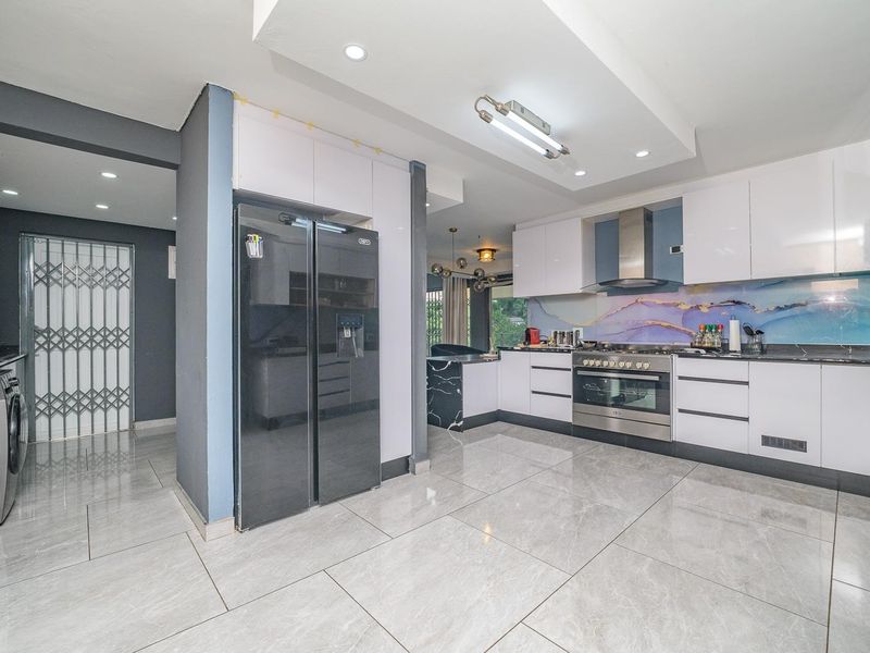 Modern kitchen featuring high-gloss white cabinetry, stainless steel appliances, a decorative splashback, and large format floor tiles with recessed lighting.