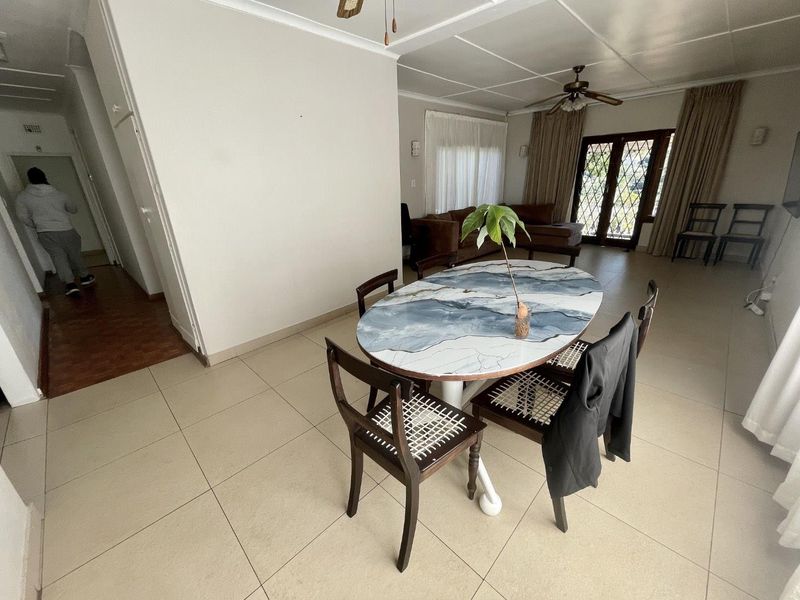 An open-plan living and dining area featuring tiled flooring, a ceiling fan, and access to the exterior through glass-paneled french doors.