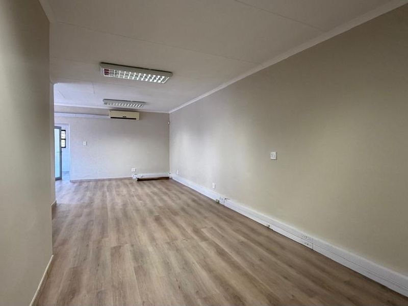 A spacious, empty office area featuring laminate flooring, integrated fluorescent lighting, and a wall-mounted air conditioning unit.
