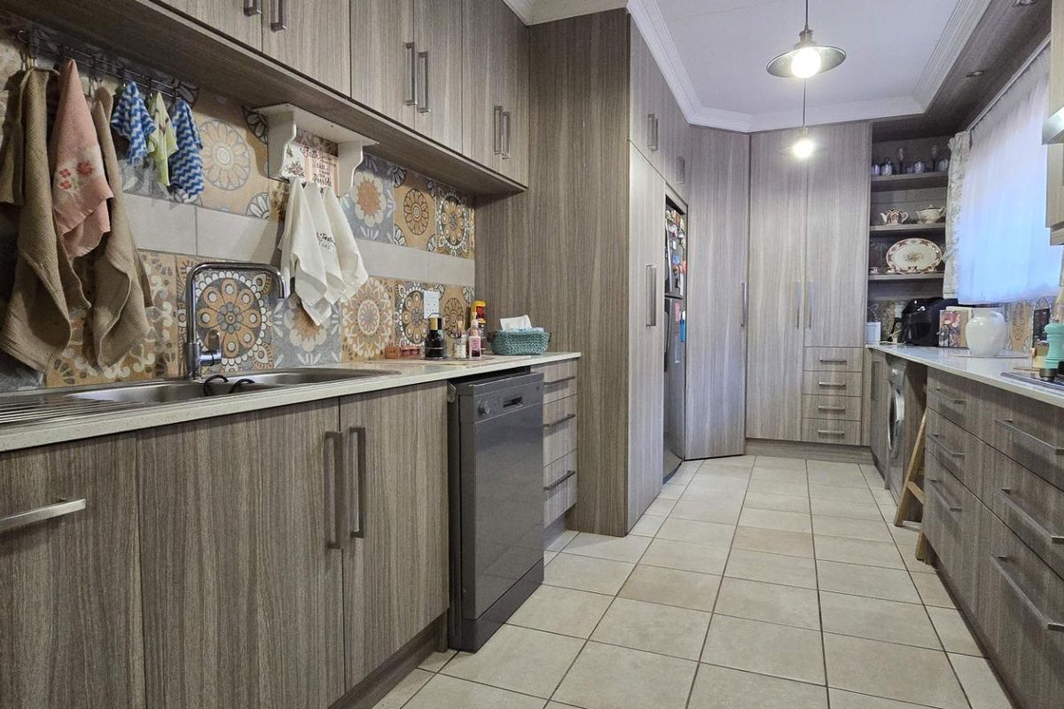 A well-appointed kitchen featuring wood-grain cabinetry, patterned tile backsplash, stone countertops, a gas hob, and integrated storage solutions.