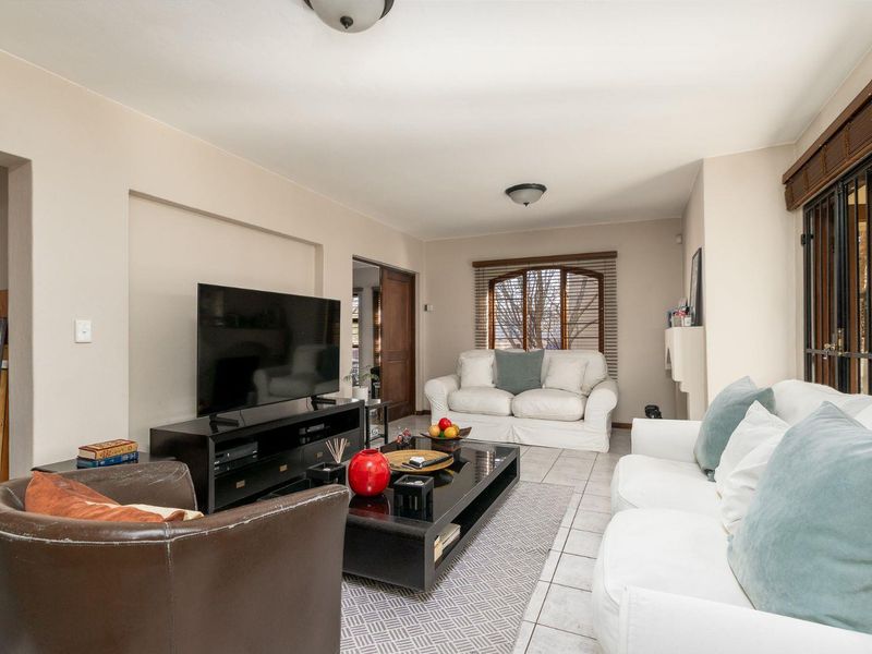 A comfortable living room featuring tiled flooring, neutral walls, and natural light through windows fitted with wooden blinds and security gates.