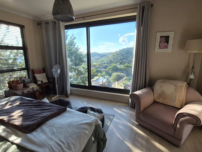 A bright bedroom featuring laminate flooring, a large window with blinds, and a sliding glass door offering scenic views of the surrounding landscape.