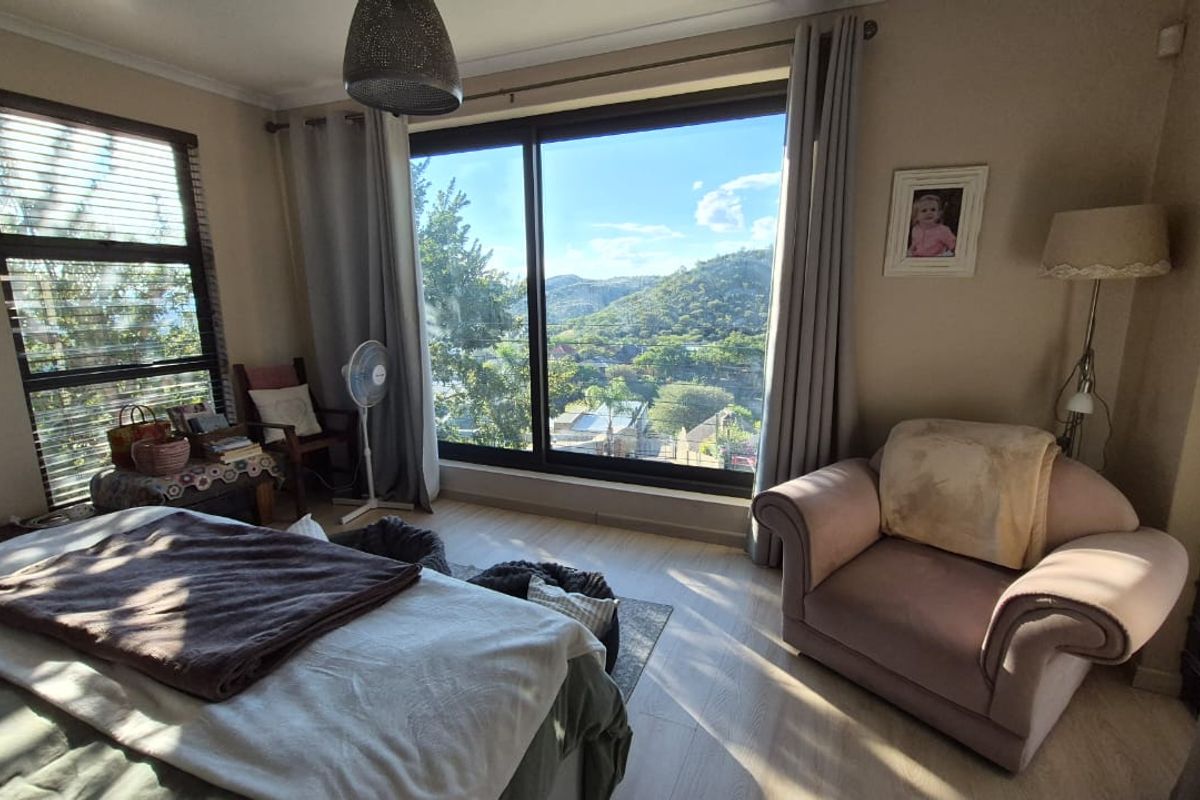 A bright bedroom featuring laminate flooring, a large window with blinds, and a sliding glass door offering scenic views of the surrounding landscape.