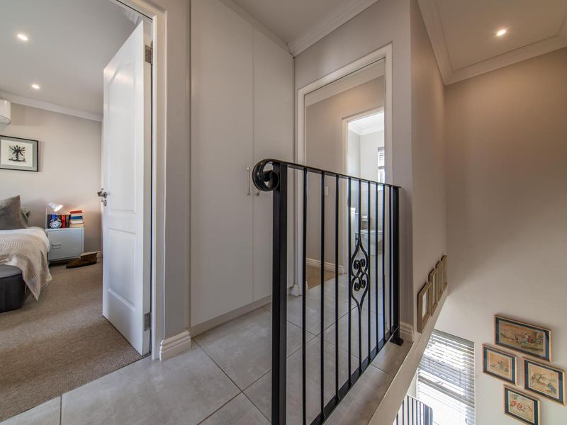A well-maintained upper-level landing featuring tiled flooring, built-in storage cupboards, and a decorative wrought iron balustrade overlooking the staircase.