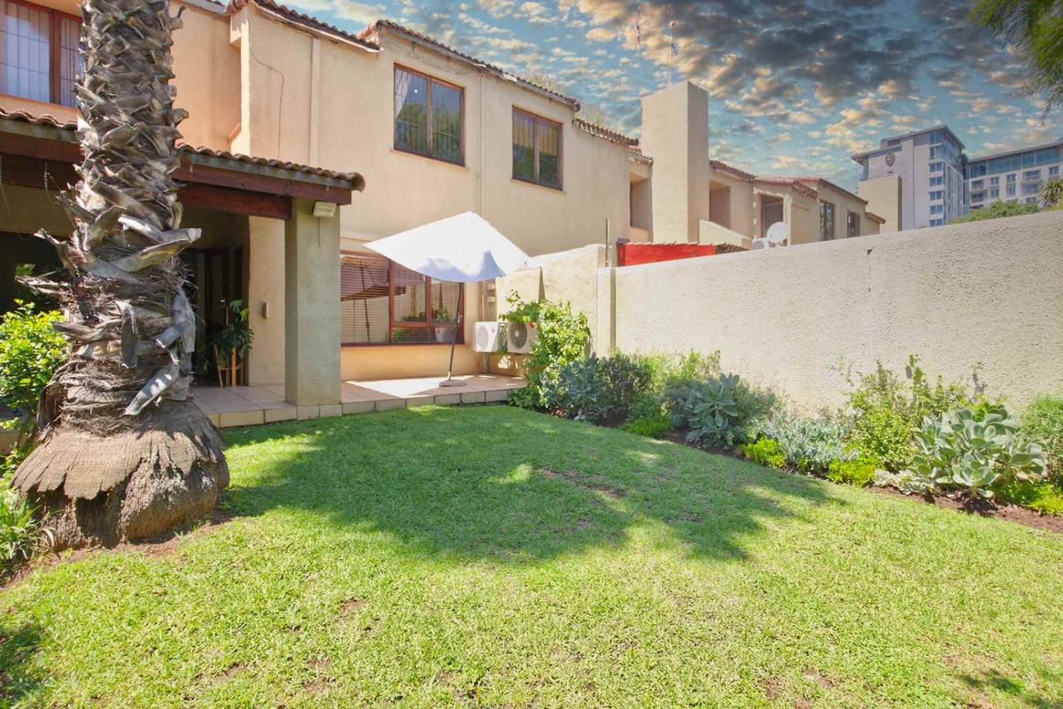 A private rear garden featuring a lawn area and a covered patio space attached to the townhouse structure.