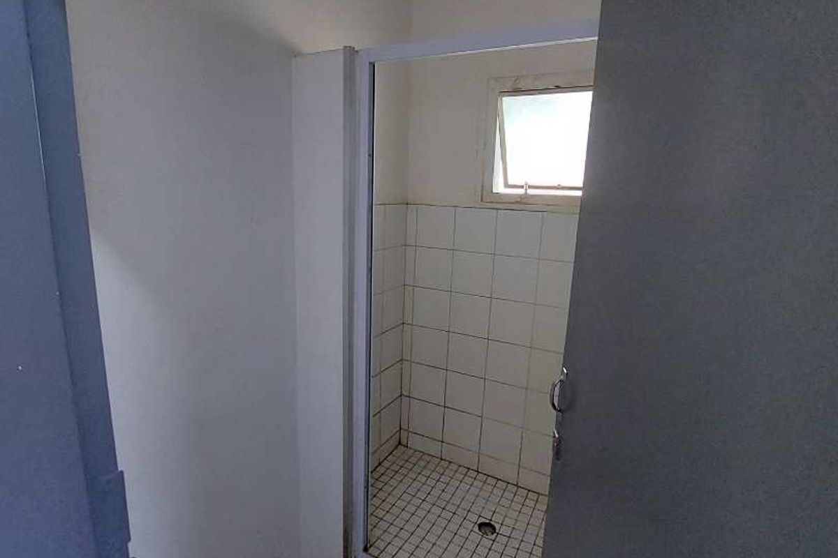 A small, empty bathroom featuring a tiled shower cubicle and tiled flooring, currently showing signs of wear and requiring cosmetic updates.