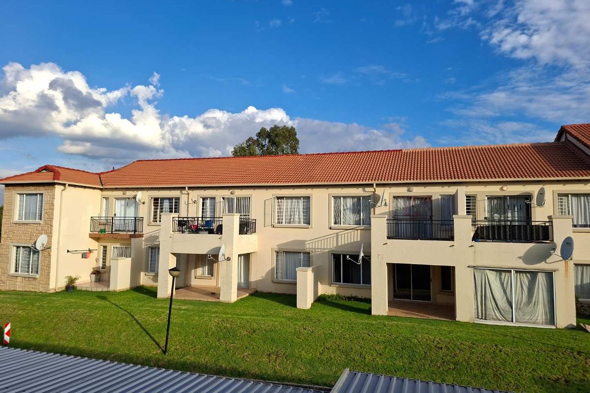 Rear view of a multi-story apartment complex featuring terracotta tiled roofing, private balconies, ground-floor patios, and landscaped lawn areas.