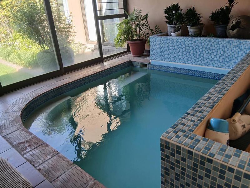 An indoor tiled swimming pool area featuring large sliding glass doors that provide natural light and access to the garden.
