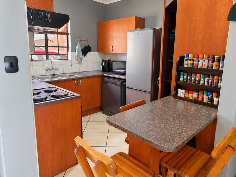 A functional kitchen featuring wood-look cabinetry, laminate countertops, a double basin sink, and an integrated electric hob with tiled backsplash.