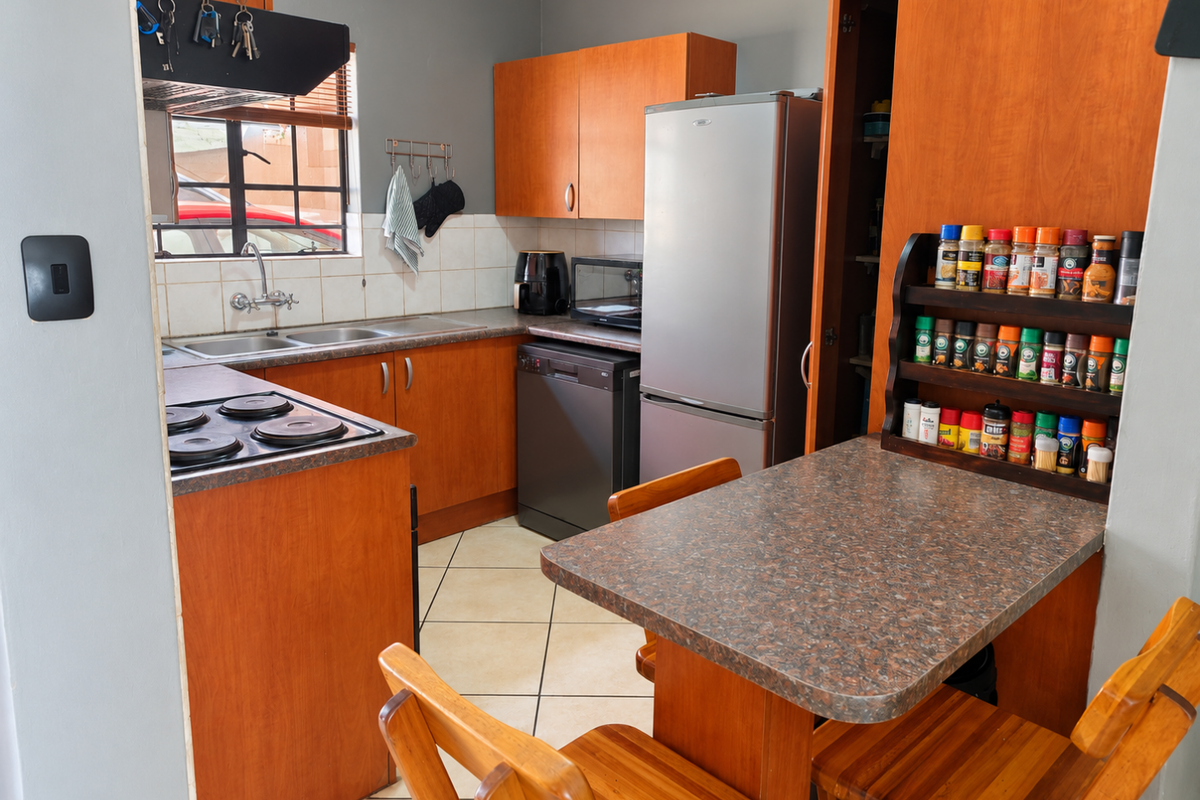 A functional kitchen featuring wood-look cabinetry, laminate countertops, a double basin sink, and an integrated electric hob with tiled backsplash.