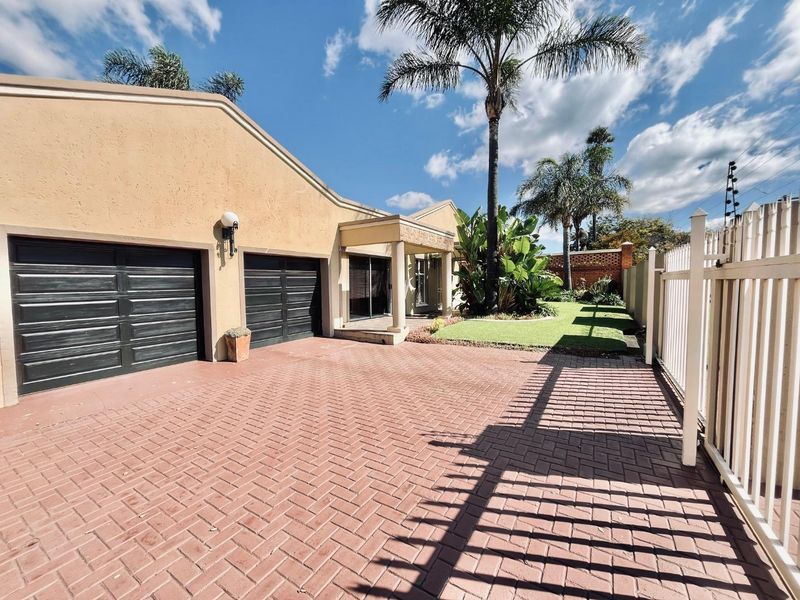 Front exterior view of the property featuring a double garage, paved driveway, covered entrance, and a well-maintained garden area.