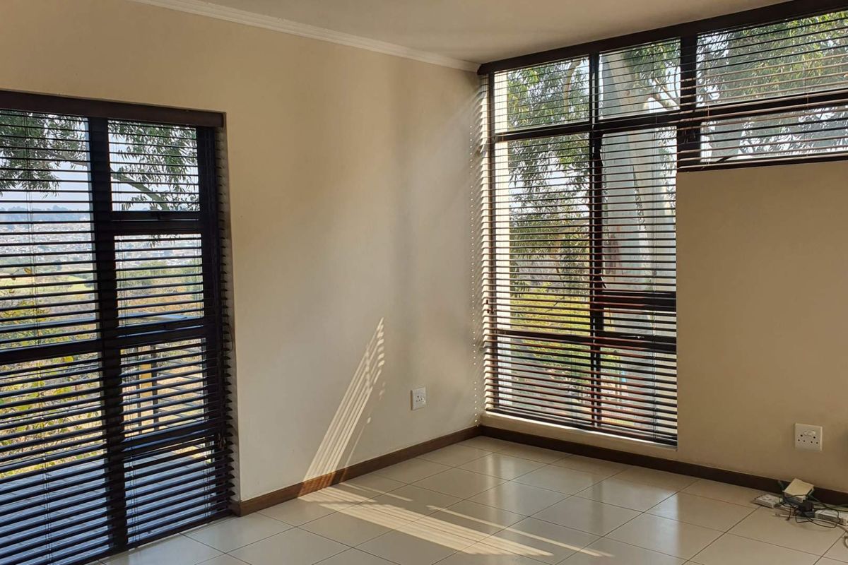 A bright, empty living area featuring large windows with fitted wooden blinds, tiled flooring, and natural light, offering a clean and versatile space.