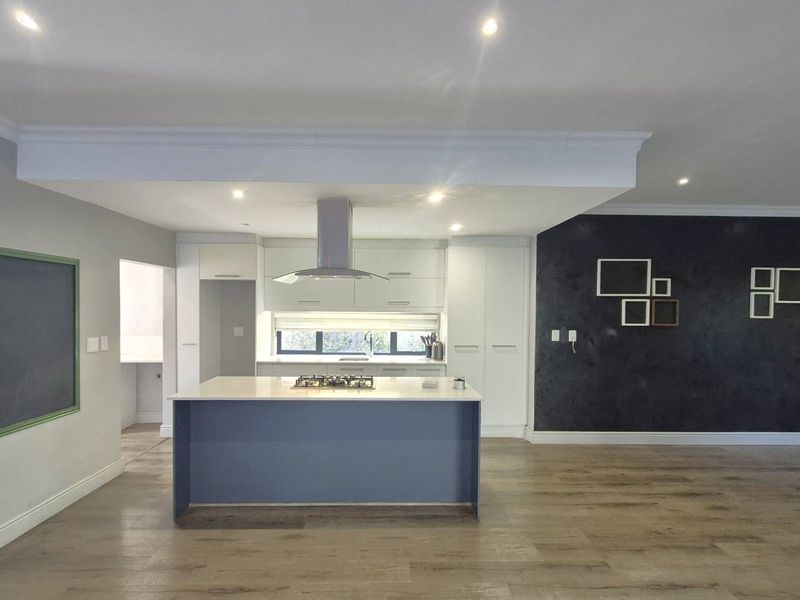 Spacious open-plan kitchen featuring a central island with gas hob, modern cabinetry, and sleek laminate flooring, creating a bright and functional living space.