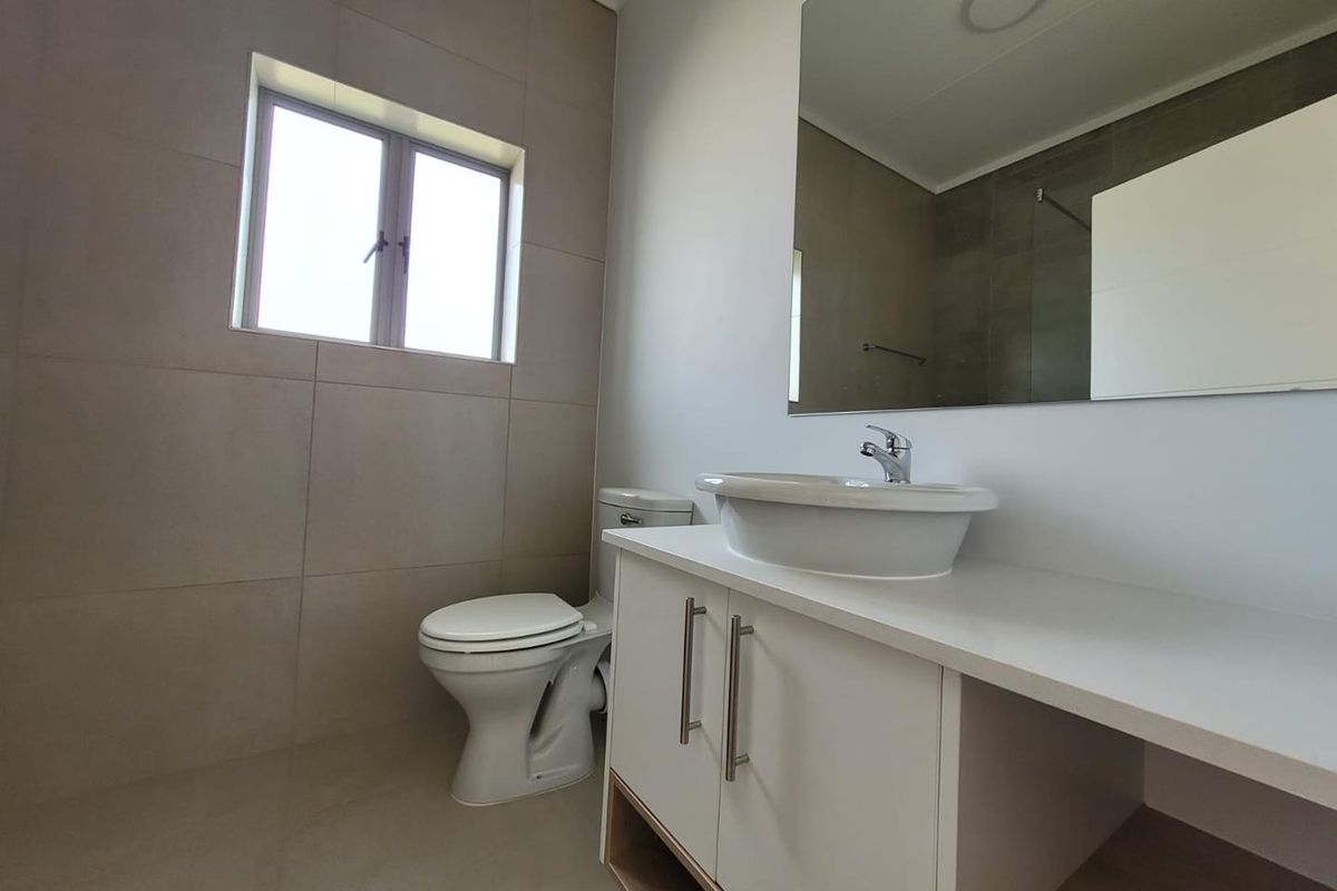 Modern bathroom featuring a sleek vanity with a vessel sink, large wall-mounted mirror, and neutral floor-to-ceiling tiling.