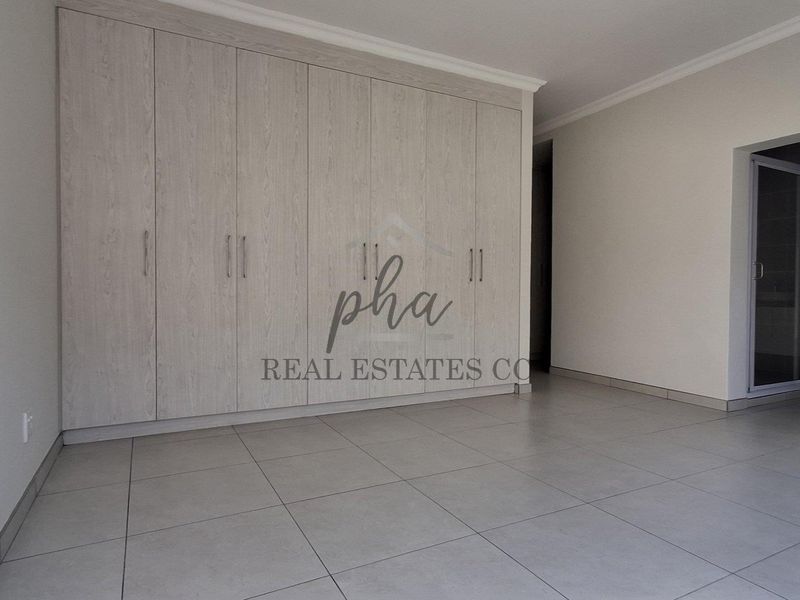 A bright, empty bedroom featuring neutral tiled flooring and extensive built-in cupboards with a modern light wood finish.