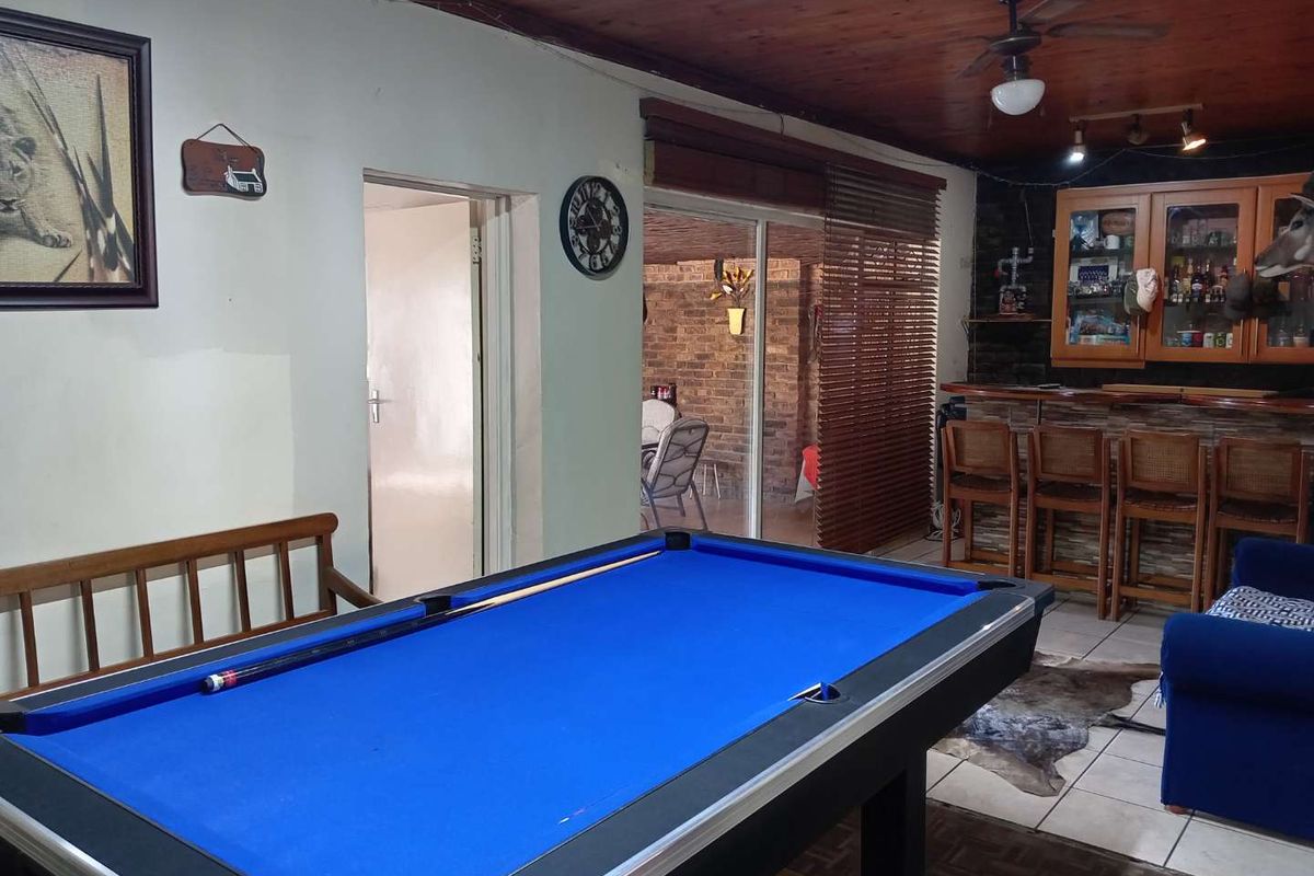 A casual entertainment room featuring a built-in bar with cabinetry, tiled flooring, and a timber-paneled ceiling, with direct access to an outdoor patio area.