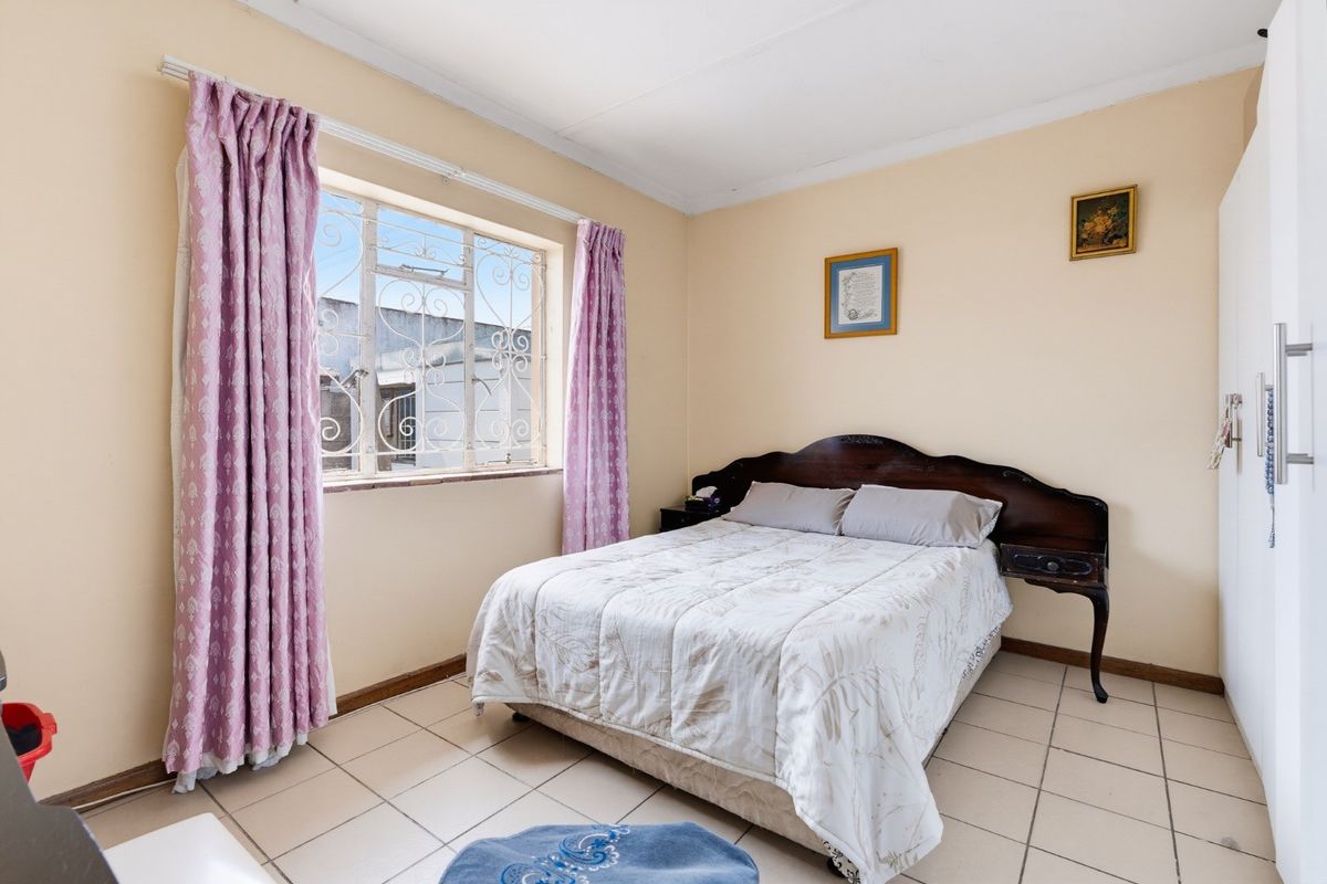 A functional bedroom featuring tiled flooring, a built-in wardrobe, and a window fitted with security bars.