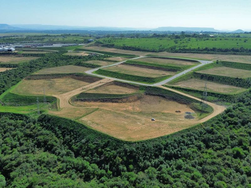 Aerial view of a large industrial development site featuring terraced plots, paved access roads, and surrounding natural vegetation.
