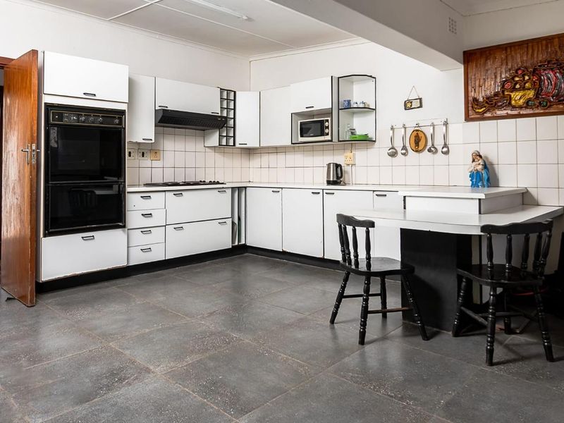 A functional kitchen featuring white cabinetry, built-in oven, hob, extractor fan, and tiled flooring with a breakfast nook area.