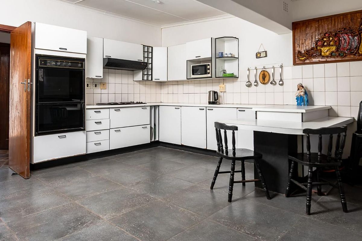 A functional kitchen featuring white cabinetry, built-in oven, hob, extractor fan, and tiled flooring with a breakfast nook area.