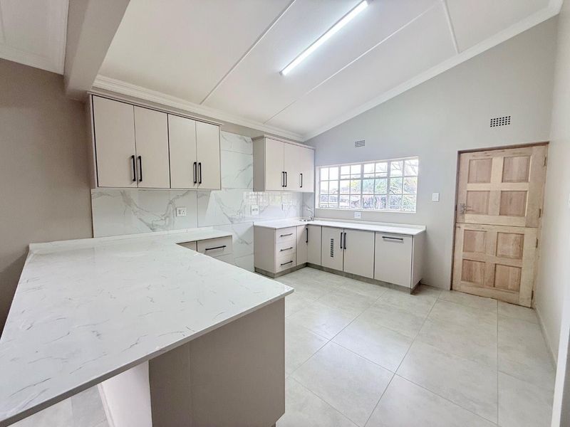 A modern, renovated kitchen featuring marble-look quartz countertops, ample built-in cabinetry, tiled backsplash, and a bright, vaulted ceiling with neutral finishes.