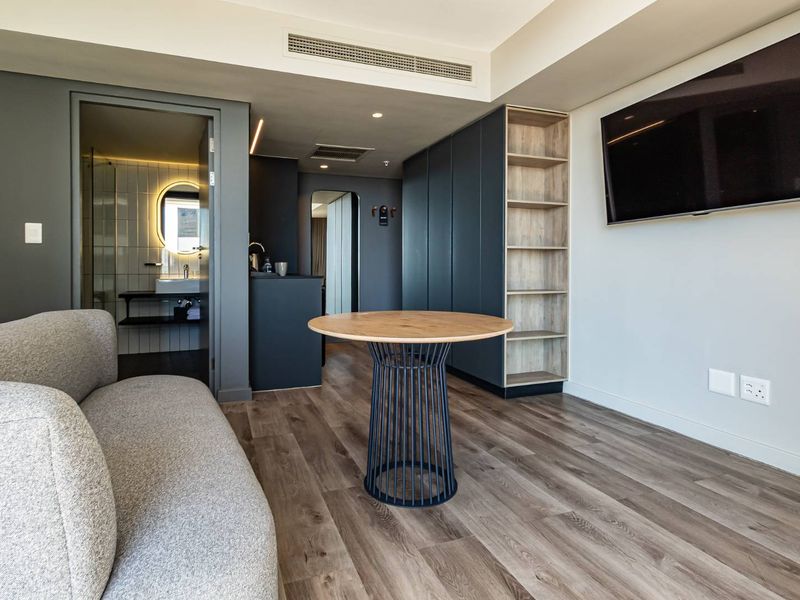Modern open-plan living area featuring wood-look flooring, built-in cabinetry with open shelving, and an integrated bathroom entrance.