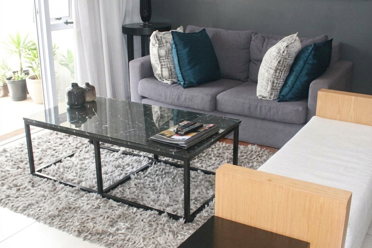 A well-maintained living room featuring neutral tiled flooring and a sliding glass door providing access to an outdoor balcony area.
