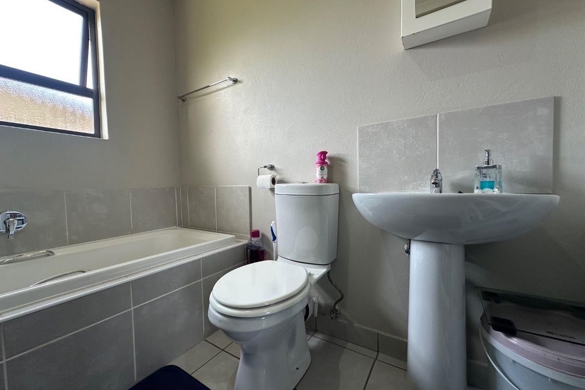 A functional bathroom featuring a tiled bathtub, pedestal basin, and toilet, finished with neutral wall tones and tiled flooring.
