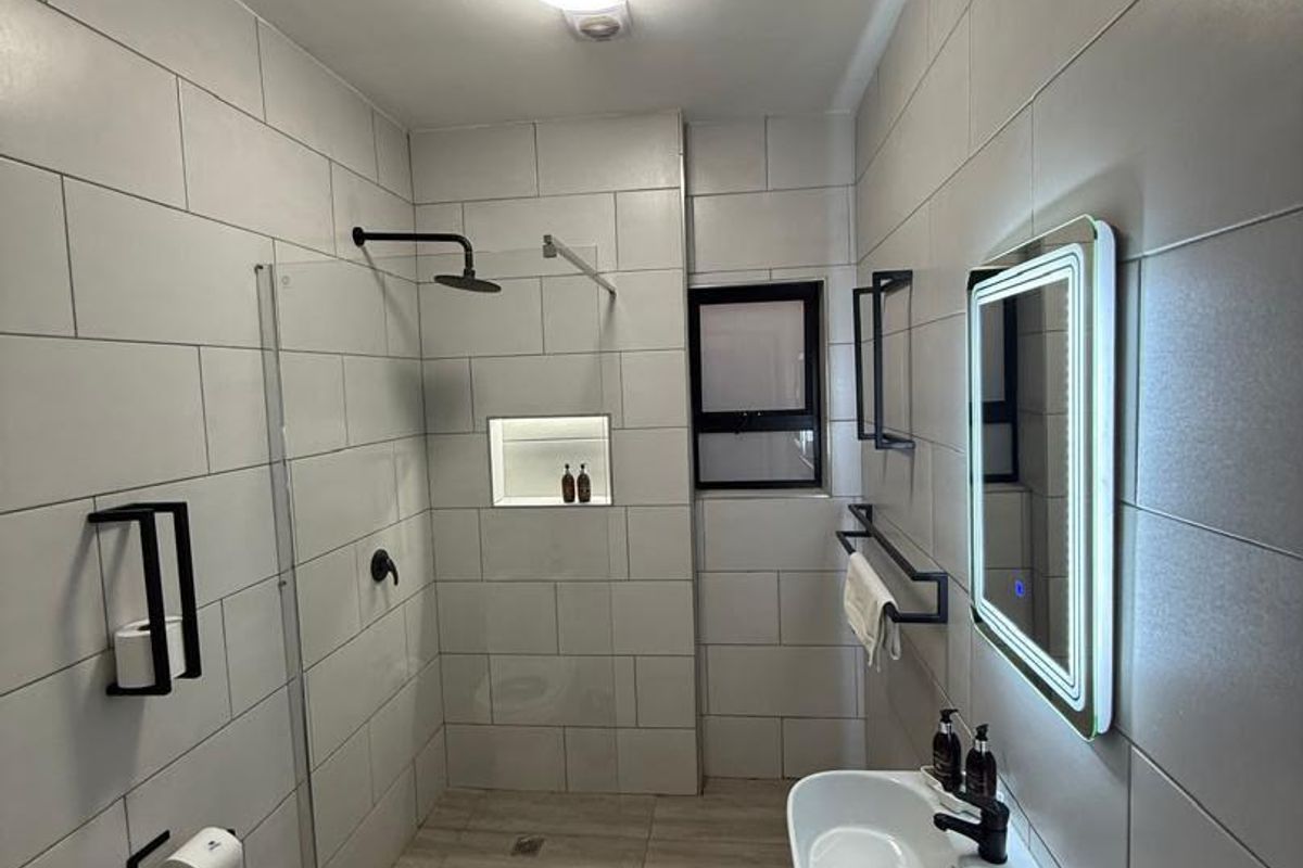 Modern bathroom featuring a walk-in shower with a recessed niche, wall-mounted basin, and a contemporary LED backlit mirror with sleek black matte fixtures.