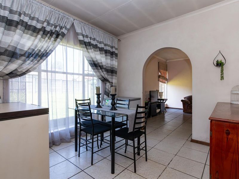 Dining area featuring tiled flooring and an arched entryway leading to an adjacent living space, with natural light from a large window.