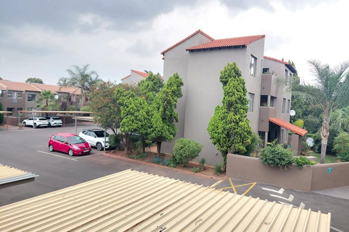 Elevated view of the apartment complex exterior, featuring multi-story residential buildings, paved parking areas, and established landscaping.
