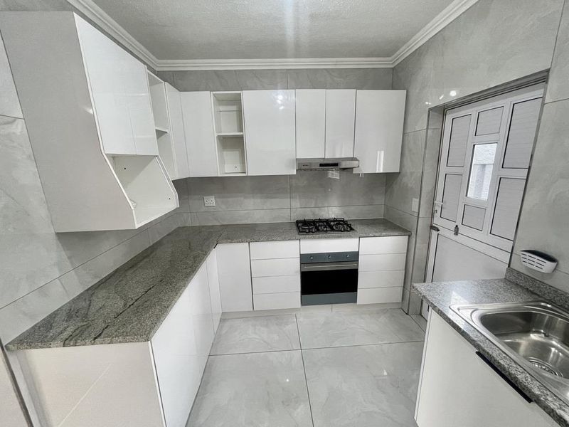 Modern kitchen featuring white cabinetry, granite countertops, built-in oven, gas hob, extractor fan, and tiled finishes throughout.