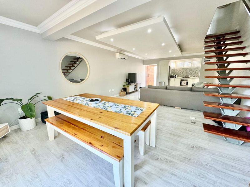 Spacious open-plan living and dining area featuring modern laminate flooring, recessed ceiling lighting, and a contemporary open-tread staircase leading to the upper level.