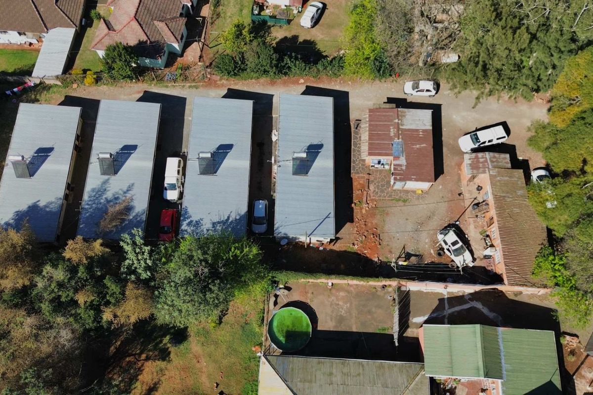 Aerial view of a residential property complex featuring multiple buildings with metal roofs, solar water heaters, and a swimming pool.