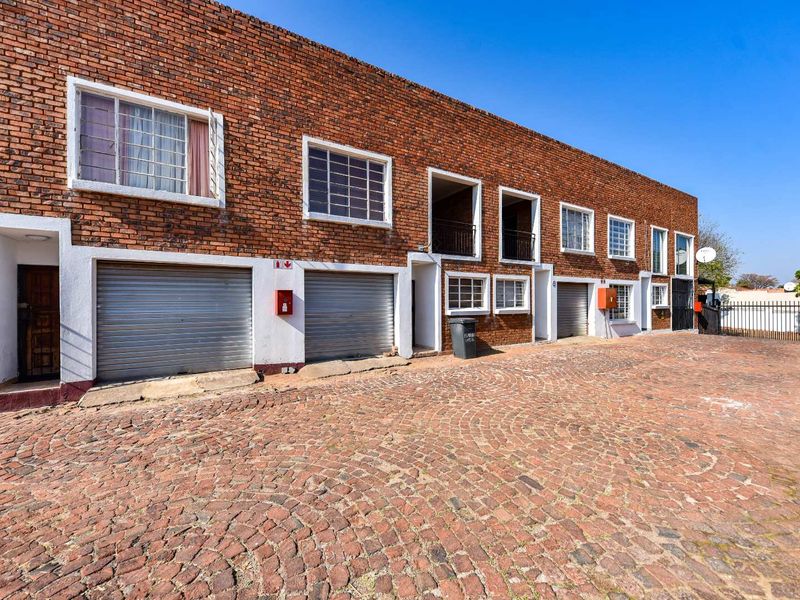 Front exterior view of a townhouse complex featuring a brick facade, multiple roller shutter garage doors, and a cobblestone driveway.