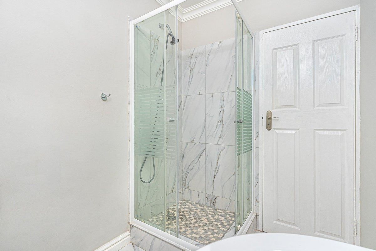 A modern bathroom featuring a glass-enclosed shower with marble-look wall tiles and a mosaic tiled floor.