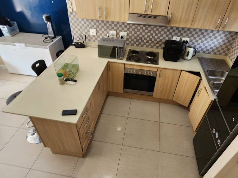 A functional U-shaped kitchen featuring light wood cabinetry, laminate countertops, integrated oven and hob, and a tiled backsplash, offering efficient workspace and storage.